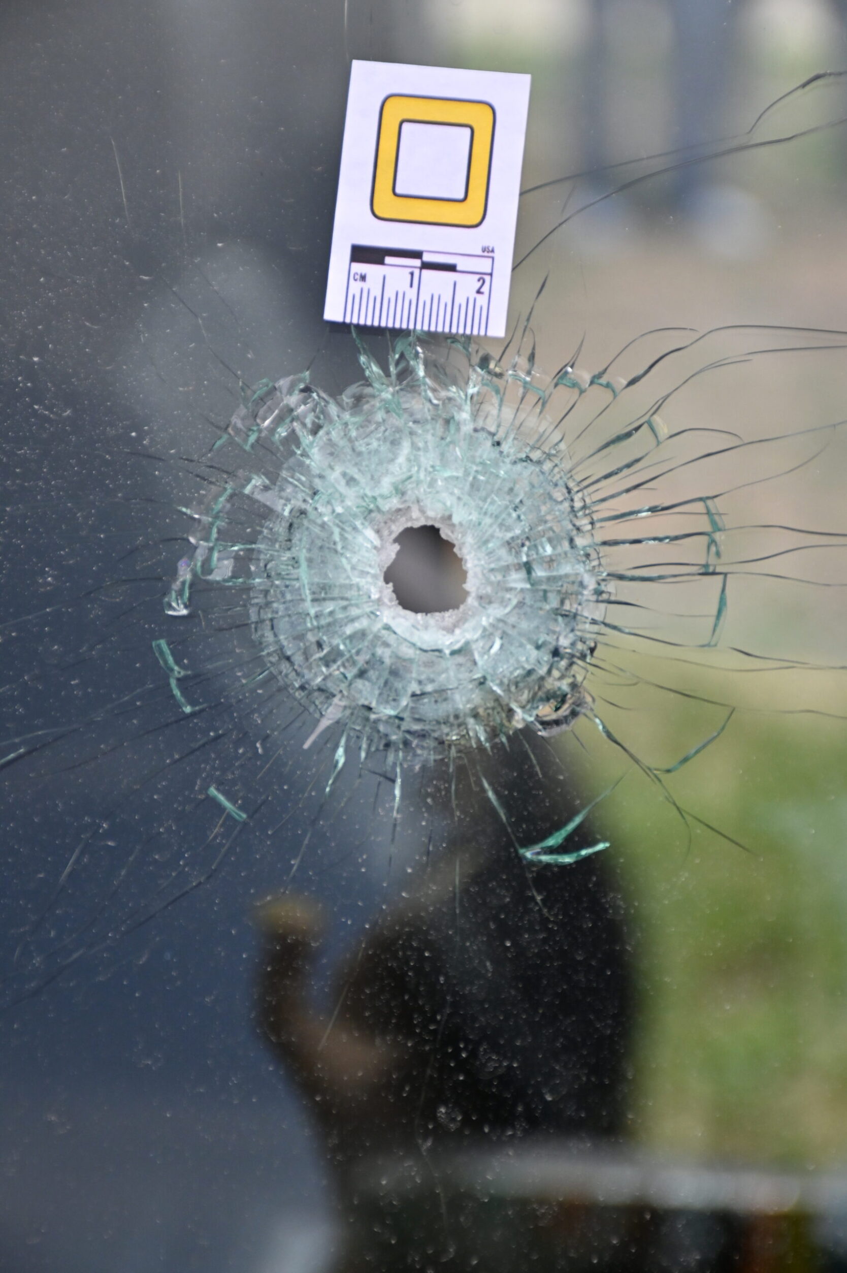 A bullet hole in glass has a maker next to it